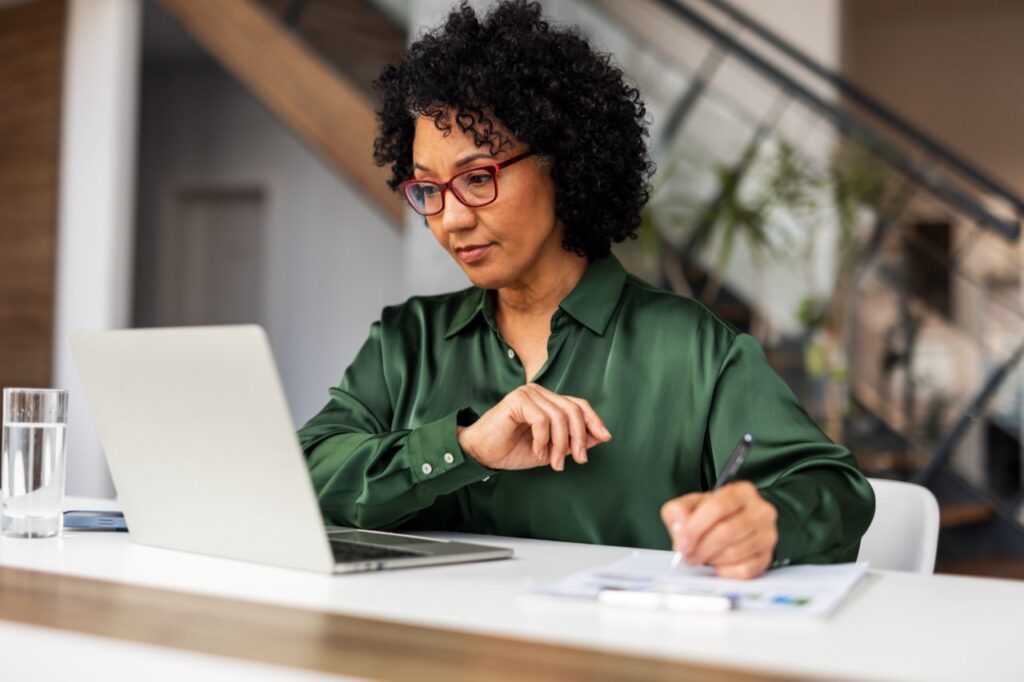 Woman in a green blouse reviewing paperwork at a laptop