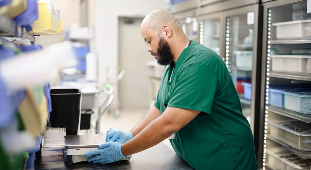 Pharmacist in green scrubs preparing medication at a pharmacy counter